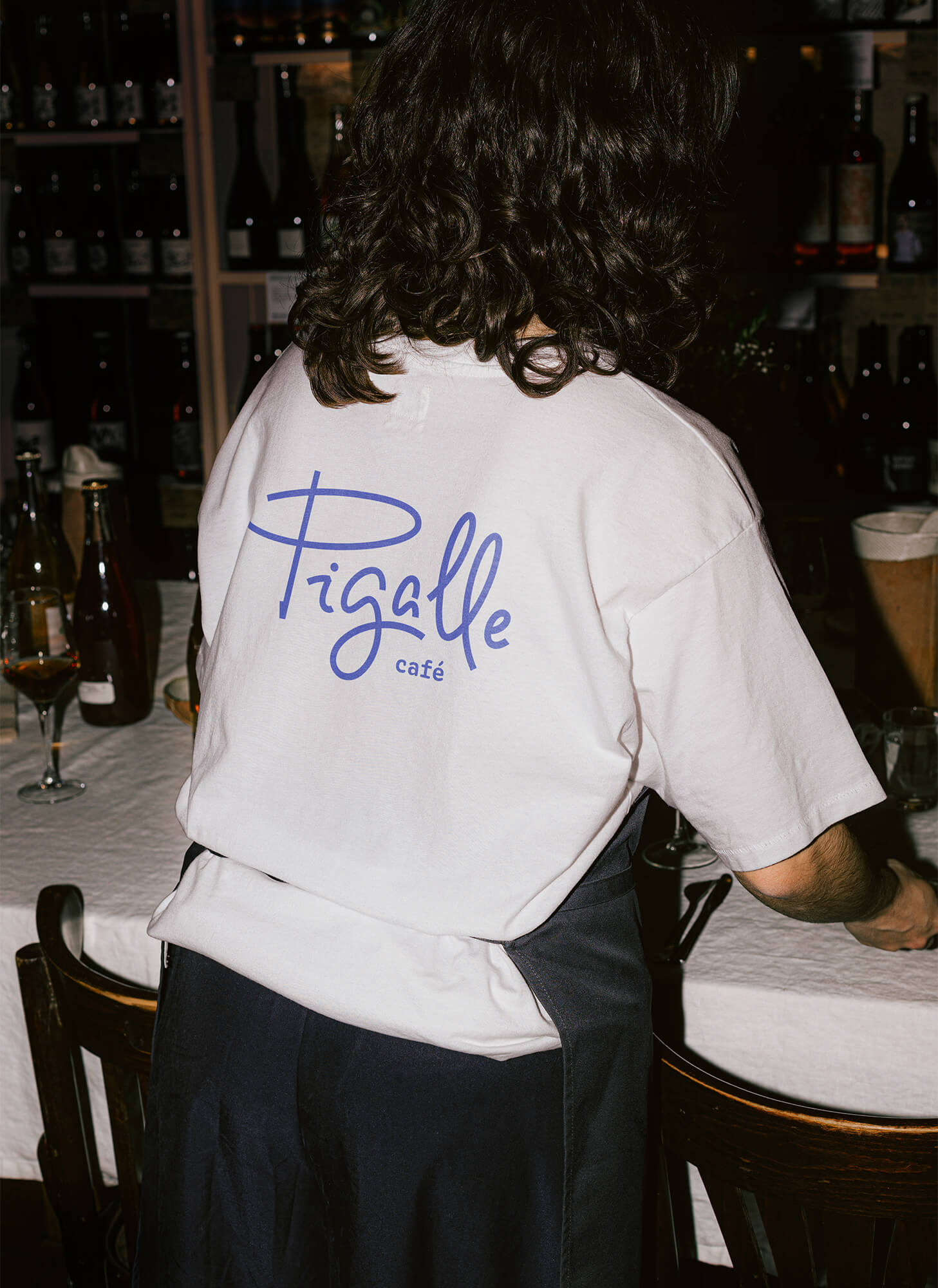 Café Pigalle's waiter waiting tables, wearing a T-shirt with the brand's logo printed on the back