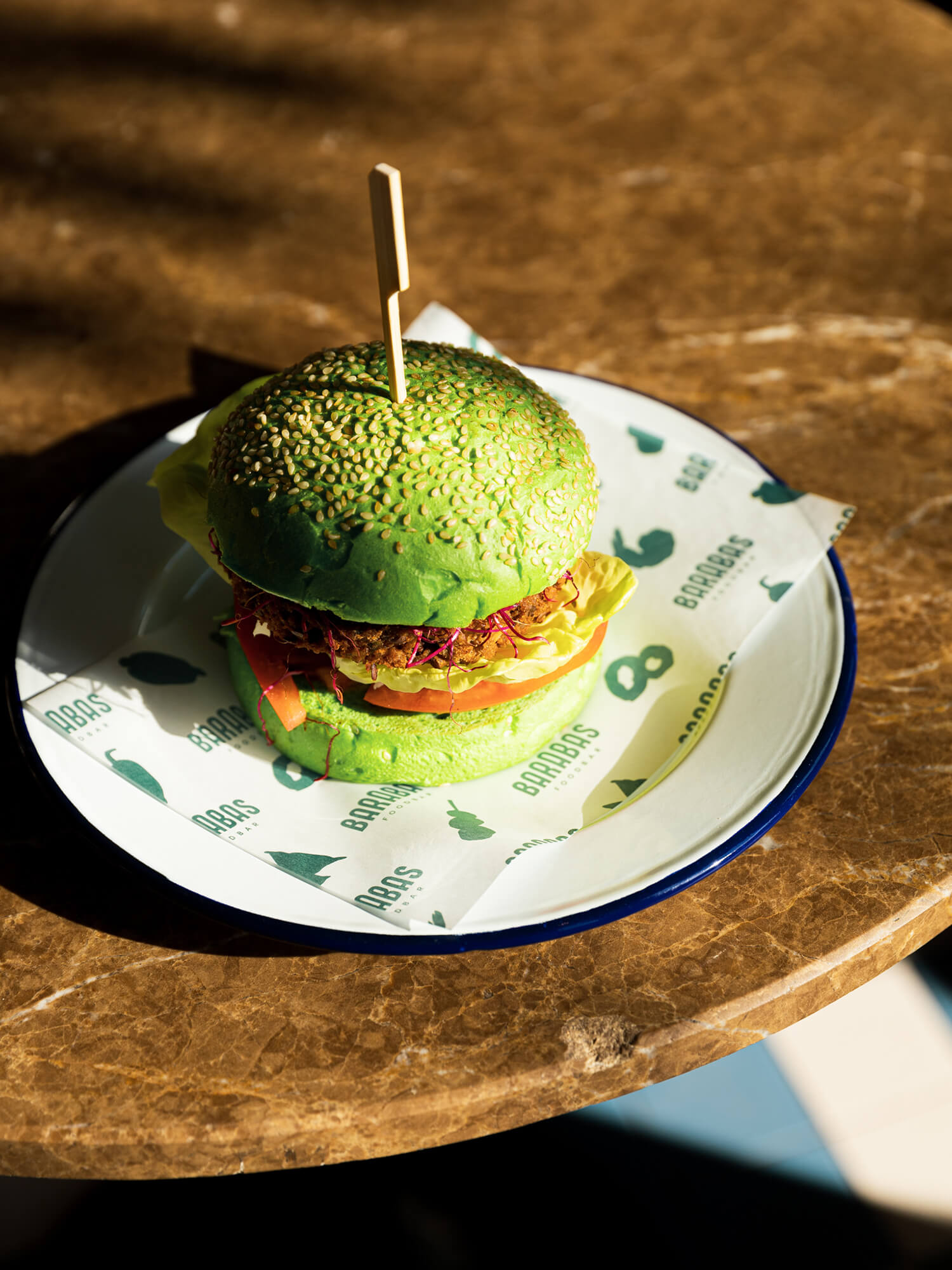 Table setting with green burger bun served on a plate with branded Foodbar Barabas deli paper