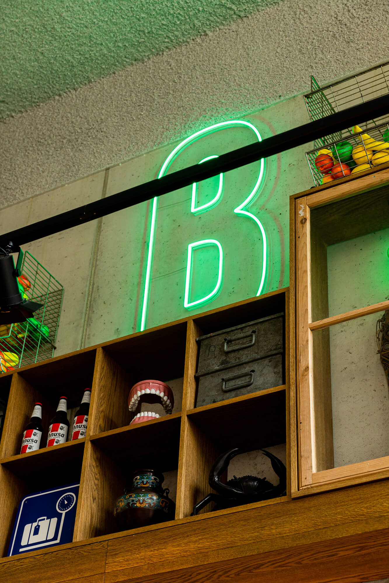 Illuminated green neon B logo signage in a cabinet inside Foodbar Barabas