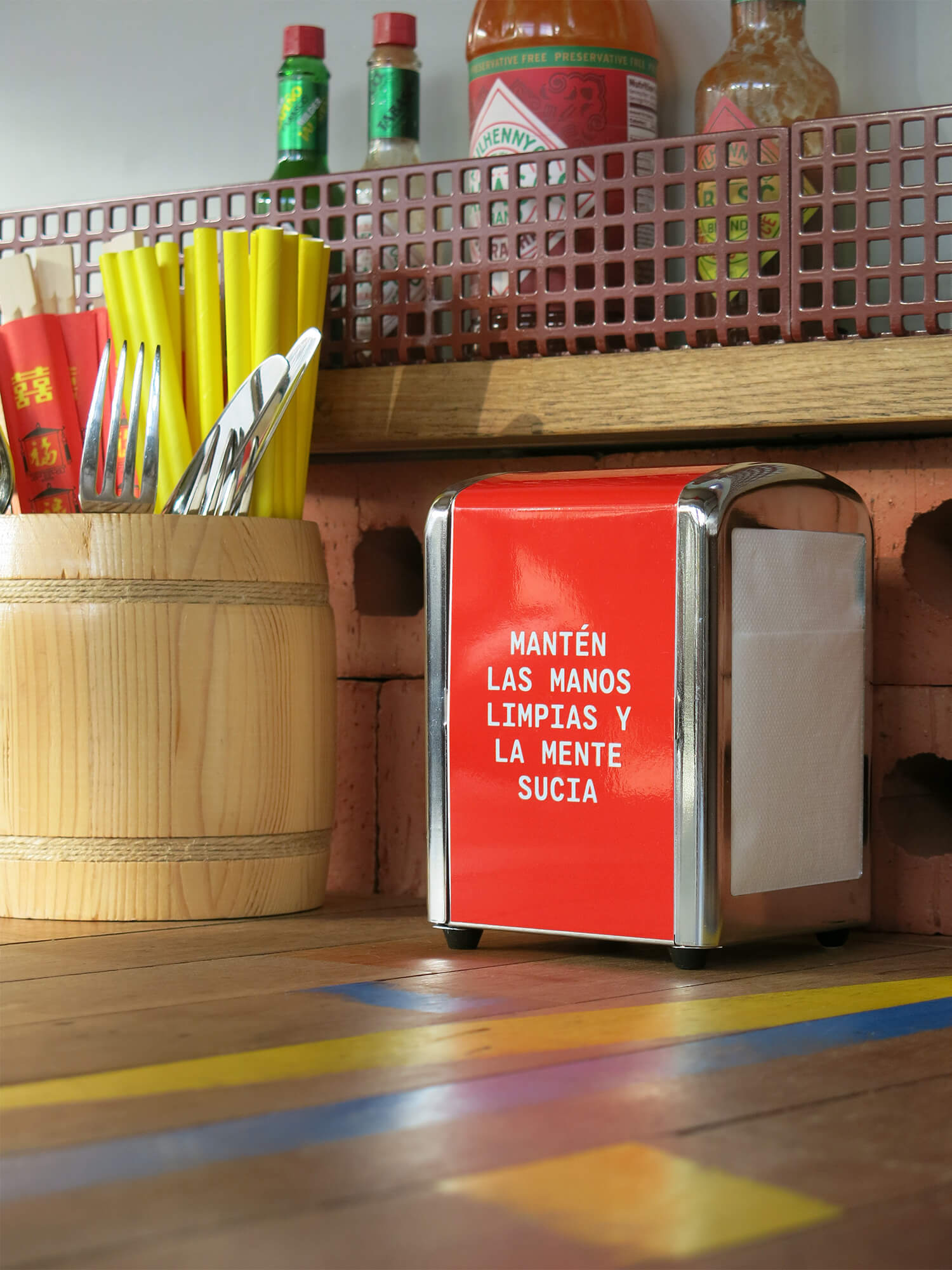 Branded napkin dispenser with quirky Spanish-language copy at Foodbar Barabas saying: 'Keep your hands clean and your mind dirty'