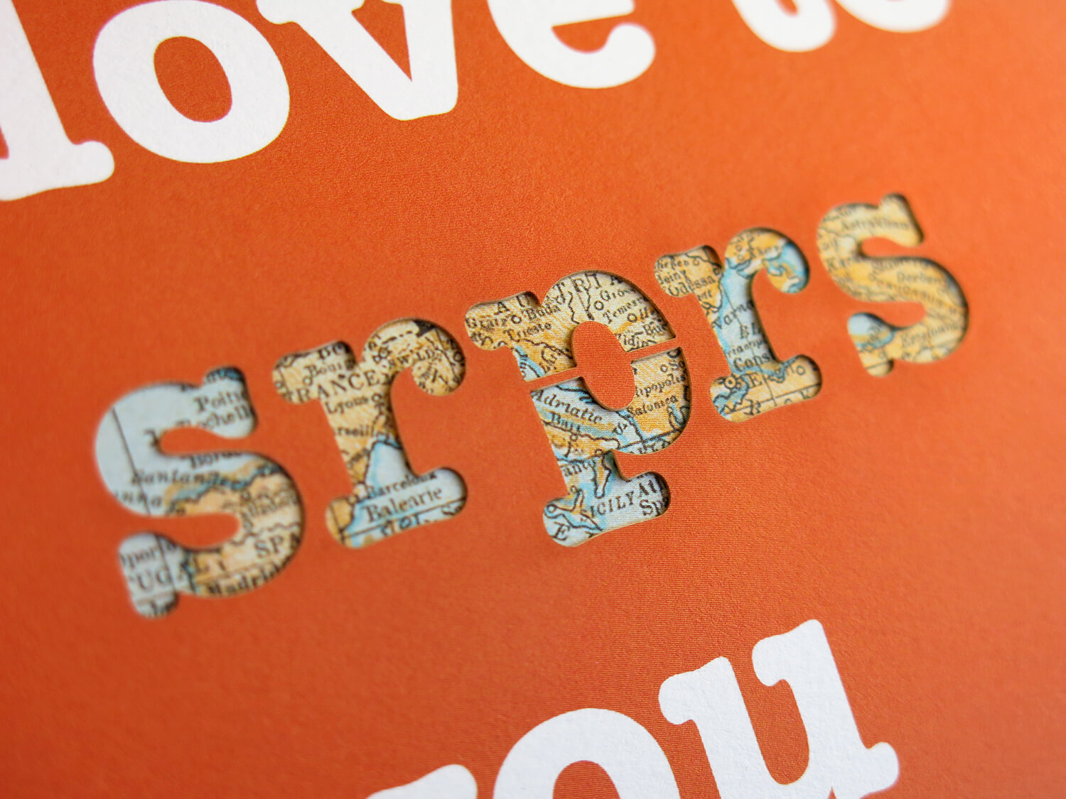 Design – srprs.me, close-up of the gift card's die-cut lettering, 'srprs' cut from orange paper revealing a vintage map underneath